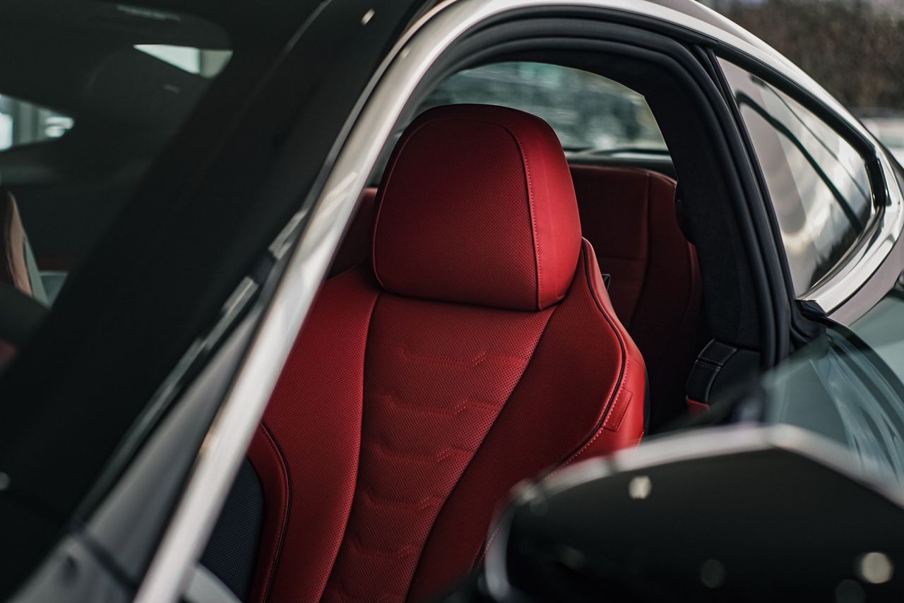 A close-up shot of a sleek car interior featuring a luxurious red leather seat illuminated by soft sunlight.